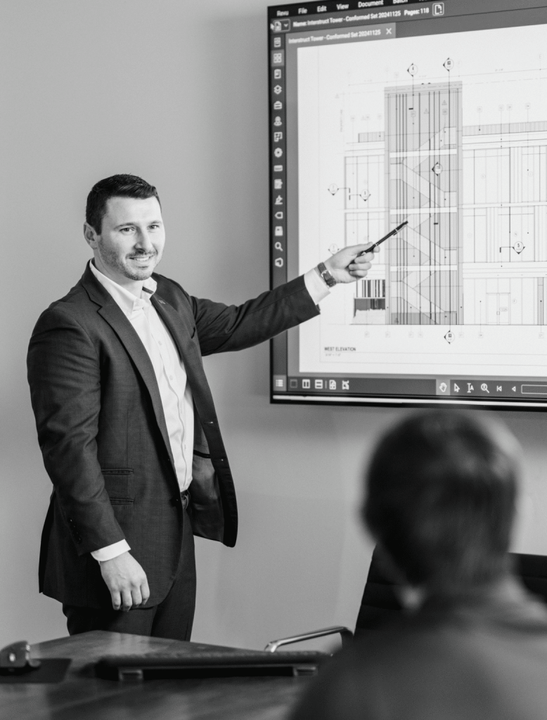 Black and white photo of Hunter pointing at blue prints on a display