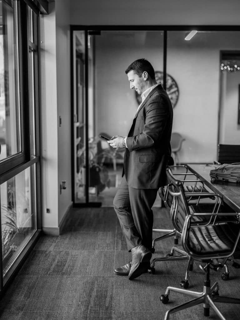 Black and white of Hunter standing at a window holding his phone