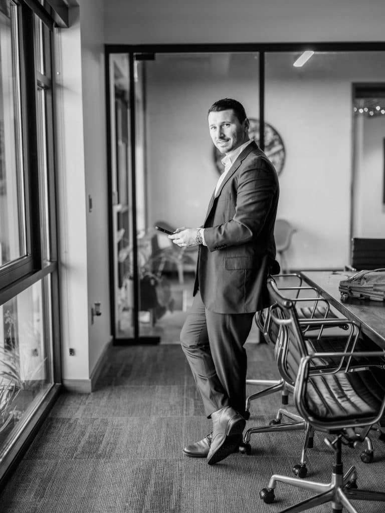 Black and white of Hunter standing at a window holding his phone